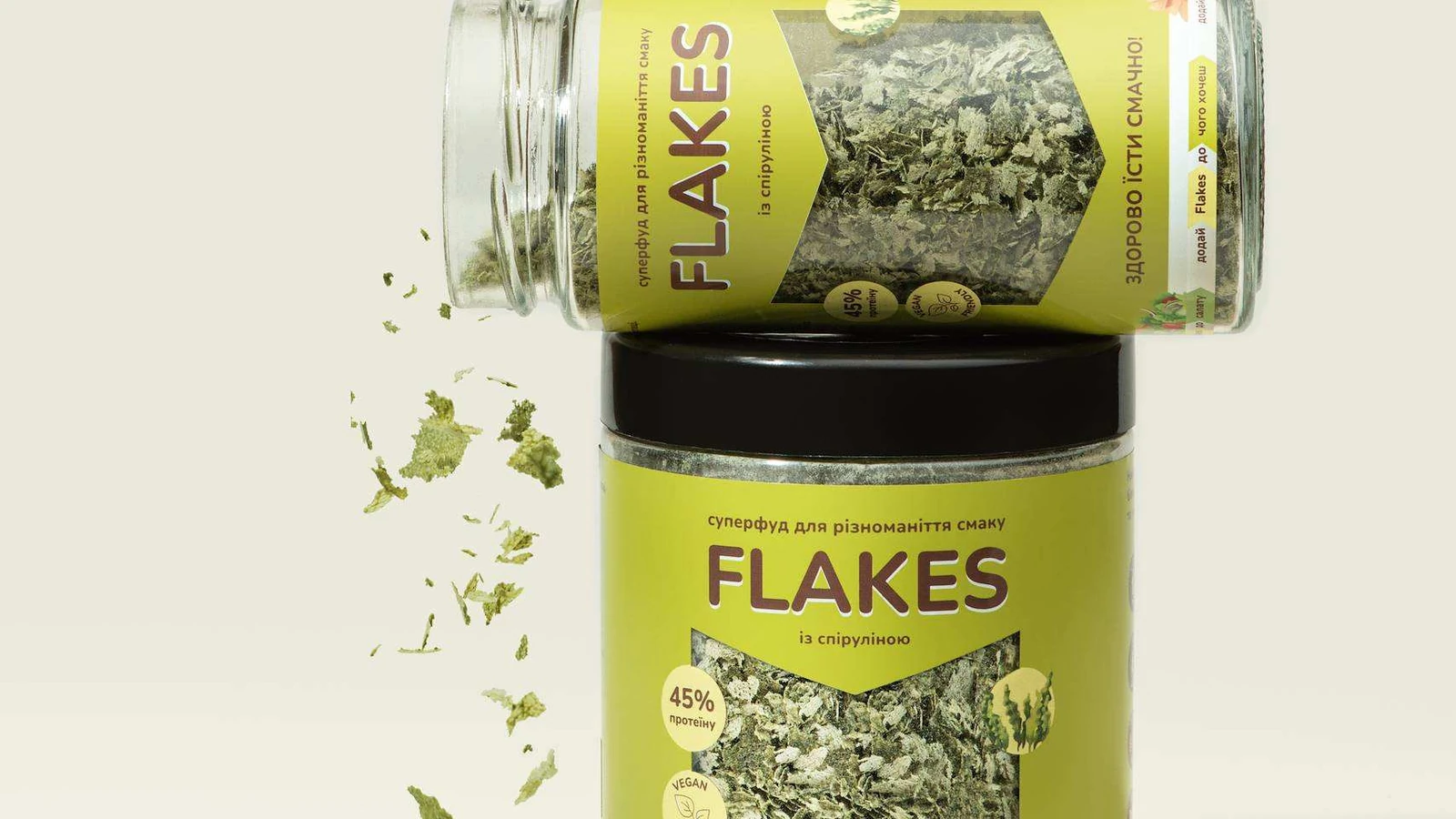 Банка Flakes зі спіруліною і зелені дріжджові пластівці, що висипаються на кремове тло